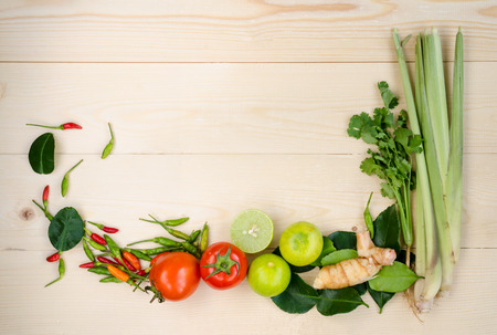 Flat lay of fresh Thai Tom Yum very delicious and famous dish's ingredients on wooden background composing of lemon grass, cilantro, galangal, kaffir lime leaves, limes, tomatoes, spicy bird peppersの写真素材