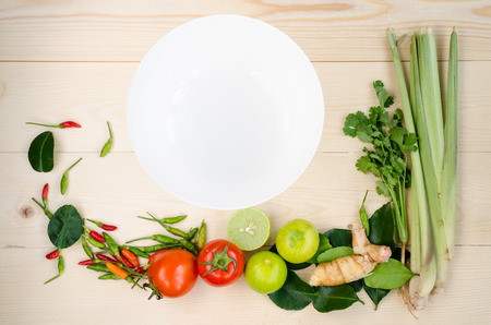 Flat lay of fresh Thai delicious spicy & sour Tom Yum dish's ingredients on wooden background of lemon grass, cilantro, galangal, kaffir lime leaves, limes, spicy bird peppers & white plate copy spaceの写真素材