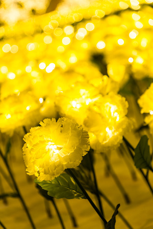 Led lights of marigold fabric handmade flower garden decorated for celebrating Christmas season and new year 2017 shining at night time, selective focus with blur yellow bokeh backgroundの写真素材