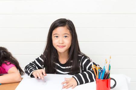 Asian happy girl with smile look forward white drawing cartoon on white paper over wall background with friendの写真素材