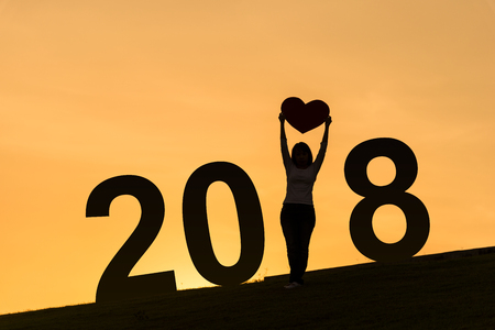 2018 new year silhouette of asian lady standing on hill and holding heart over her head with two hands during sunset time to show her loveの写真素材