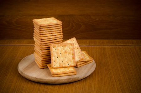 Fresh baked cream crackers in stacks over wooden cutting circle board on wood table and dark brown background with copy space for text decorationの写真素材