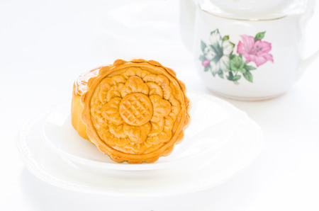 Moon cakes of flower design over white plates to celebrate Chinese moon festival on white table with tea pot with copy spaceの写真素材
