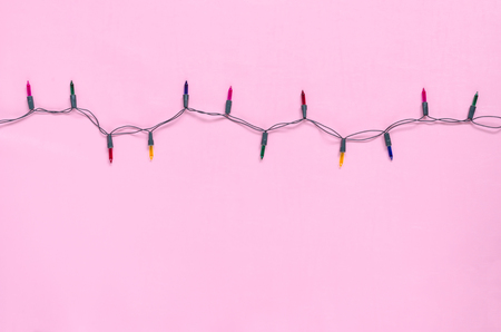 Christmas light bulbs on string in multi colours; blue, yellow, red, pink & green on pink background with copy space for Xmas text decoration, new year or special event celebration (tree ornament concept)の写真素材