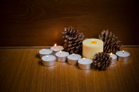 Lid yellow and white candles with pine cones over teak wood table and wall background at night time with copy space for text or wordings decoration, warm xmas or special event celebration conceptの写真素材