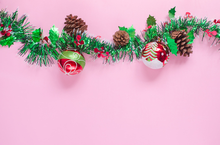 Christmas decorative red balls painted with white snow, green pine tree and cone, white curved circle lines & green big line on pink background and space with green white shiny decoration for xmas treeの写真素材