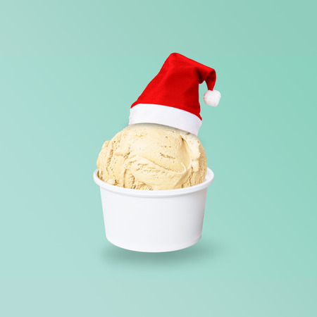 Santa Claus red hat on real vanilla ice cream scoop in paper cup isolated on green background  to celebrate Christmas holiday season, new year party or special eventの写真素材