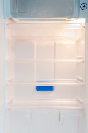 Opened and empty inside white refrigerator background of regular cool shelf and frozen section for storing food, fruits, drinks, vegetables, with light on and button for temperature adjustmentの写真素材