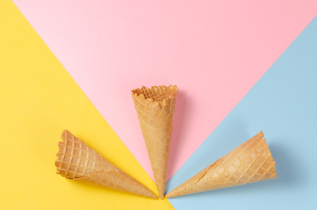 Ice cream waffle cones over light yellow, sweet pink and light blue background with copy space for text, logo or wordings insertion or decoration, colourful summer cold sweet snack conceptの写真素材