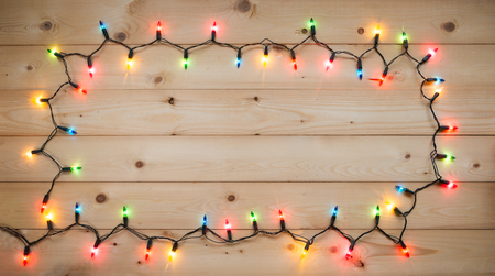 Christmas light bulbs turned on or lid on string as frame in blue, yellow, red, pink, orange and green vintage style on wood background at night time, Xmas or new year holiday decoration ornamentの写真素材