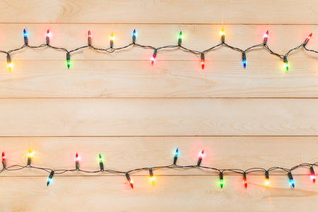 Christmas light bulbs were turned on or lid on string in multi colours; blue, yellow, red, pink, orange and green on light wooden background at night time, Xmas or new year holiday decoration ornamentの写真素材