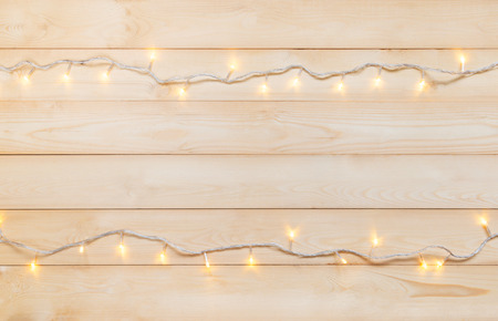 Christmas lights in warm yellow white on string over light wooden background with copy space at center for text, logo decoration on Xmas eve celebration, special holidays, new year eventの写真素材