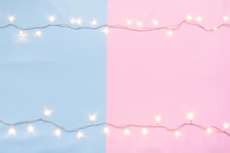 Christmas lights in warm yellow white on string over light pink & blue background with copy space at center for text, logo decoration on sweet Xmas eve celebration, love special holidays or new yearの写真素材
