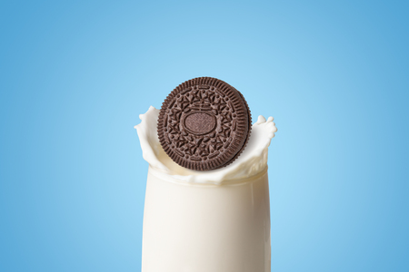 Cookies and cream of chocolate flavour with a sweet creme filling dropped in fresh milk splash in clear glass isolated on blue background (clipping path included), American famous snack brandの写真素材