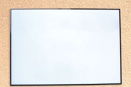 White blank advertising sign with black frame hanging outside at the exterior wall of a buildingの写真素材