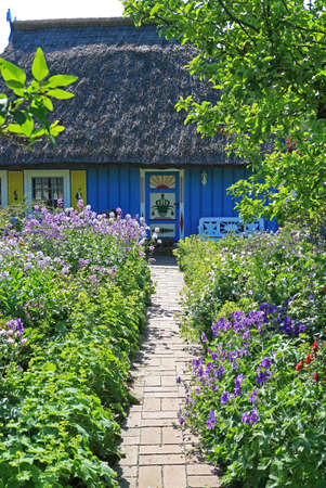 Footpath through beautiful flowerbeds to an old wooden house with a thatched roofの写真素材