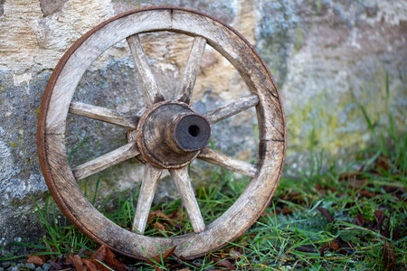 Vintage wooden cartwheel leaning against stone wallの写真素材
