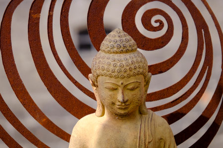 Small Buddha statue in front of a spiral of rusted iron