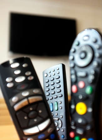 Group of TV remote controls with a TV at the background
