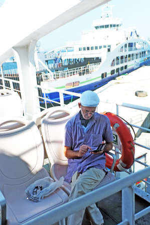 Elderly passenger plays with his smart phone while waiting the departure of the ferryのeditorial素材