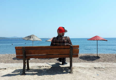 Elderly man sitting on a bench by the beachのeditorial素材