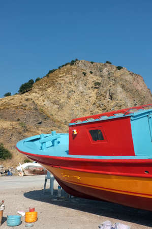Colorful small boat painted on dry land in front of rocky hillの写真素材