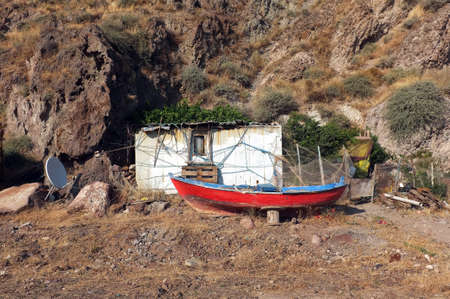 Little hut and a red boat in front of rocky hillの写真素材