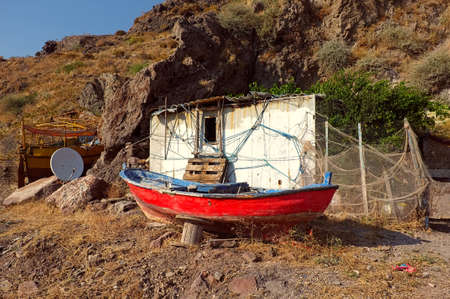 Little hut and a red boat in front of rocky hillの写真素材