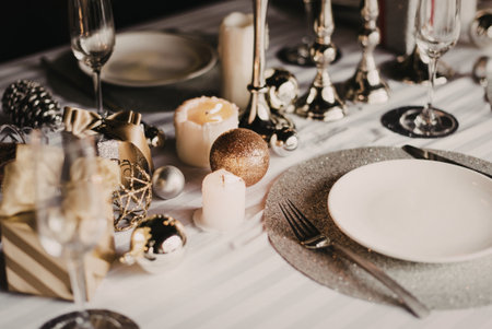 Christmas table setting with plates and cutlery, candles and golden decorationsの素材