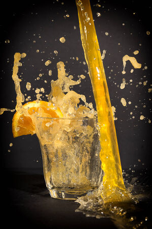 Orange flavoured soft drink with splashes in a glass with a dark background.の写真素材