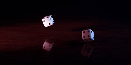 Dice with a red tint on a reflective surface and dark background.の写真素材