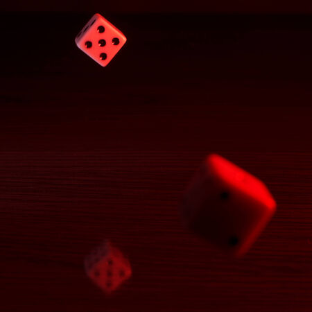 Dice with a red tint on a reflective surface and dark background.の写真素材
