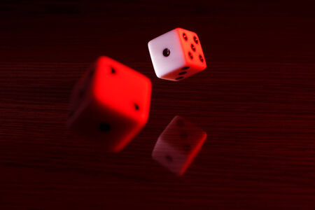 Dice with a red tint on a reflective surface and dark background.