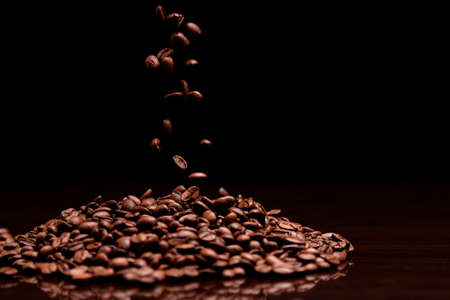 High contrast image of coffee beans being dropped onto pile with black background.の写真素材