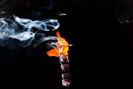 Pink Marshmallows on fire with flames and sparks with a black background.