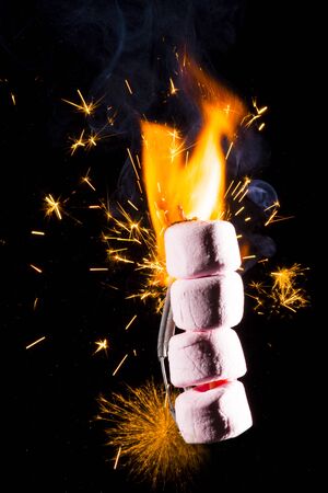 Pink Marshmallows on fire with flames and sparks with a black background.
