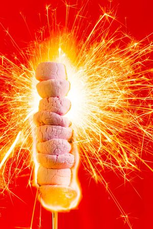 Pink Marshmallows on fire with flames and sparks with a red background.の写真素材