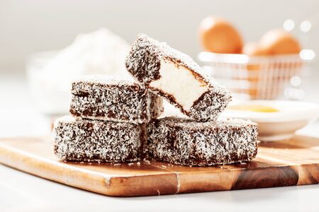 Group of Lamingtons on a timber cutting board with food ingredients in the backgroundの写真素材