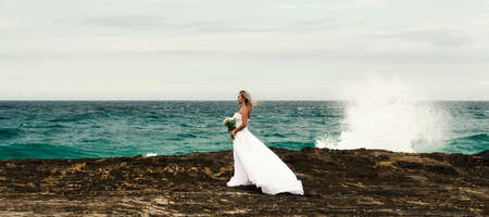 Beautiful bride at the beach with a flower bouquet.の写真素材