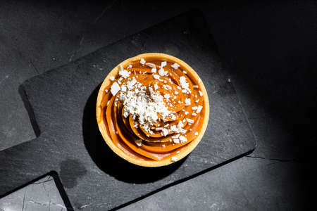 Detailed close up of a caramel tart with white chocolate flakes