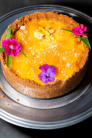 Homemade mango and coconut cheesecake with fresh edible flowers.