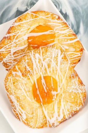 Fresh baked apricot and custard danish topped with white fondant and icing sugar.の写真素材
