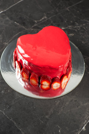 Beautiful heart-shaped moist mud cake with a ganache coating, red mirror glaze, and a fresh strawberry border.の写真素材