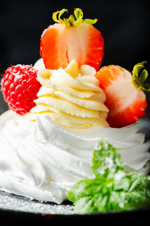 Crispy baked Italian meringue with a marshmallow center, filled with Chantilly cream, topped with fresh strawberries and raspberries.の写真素材