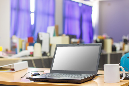 A laptop computer on a wooden desktop with a hot coffee cup in office, selective on cup.