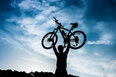 biker is holding bicycle above his head at sunrise.の写真素材