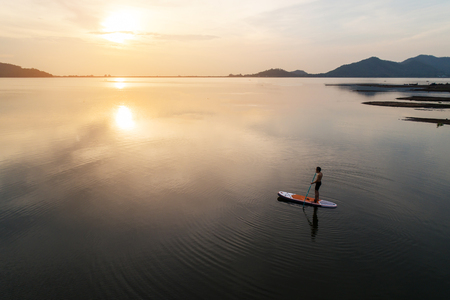 Silhouette Aerial view of stand up paddle boarder paddling at sunset on a flat warm quiet river.のeditorial素材
