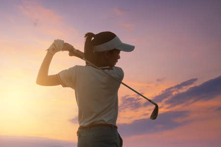 Young Women Asia player golf swing shot on course with sunset sky twilight background. exercise and health concept. Golf practice to be a professional golferの写真素材