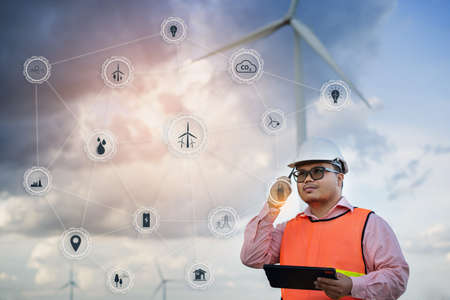 Male Engineer holding tablet with save world icons in Wind Mill Power Generator Station and wind...