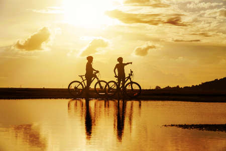 Young Couple in love fun and happy riding mountain bike after covid-19 coronavirus outbreak. End of the coronavirus outbreak. Silhouette cycling man and woman riding mountain bike at sunset time.の写真素材
